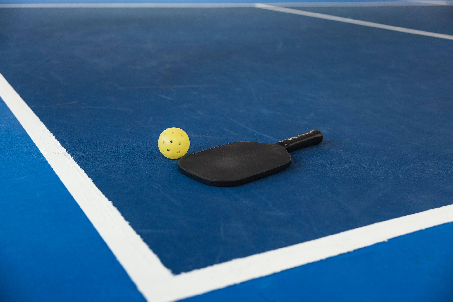 Pickleball paddle and ball on court surface, essential equipment for UK pickleball players
